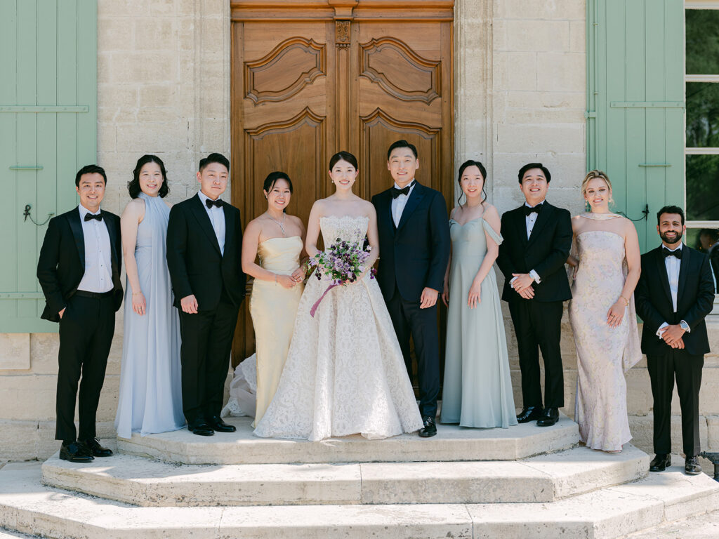 Casey and James pose with their wedding party before the carved wooden doors of Château de Tourreau.