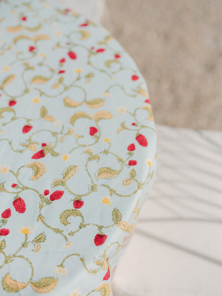 Close-up of a pale blue tablecloth embroidered with red strawberries and botanical motifs for the Provence welcome party.