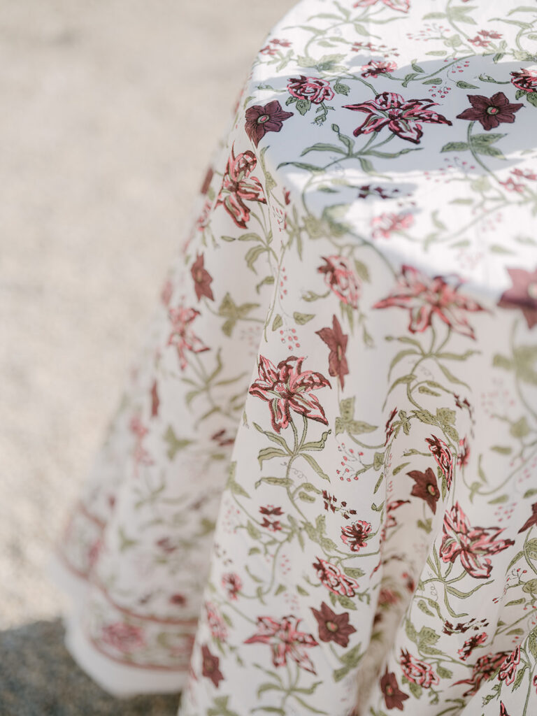 Detail of a cream tablecloth patterned with burgundy, pink and green garden flowers for the outdoor welcome reception.