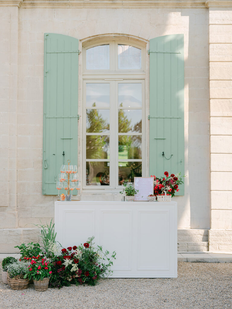 White cocktail bar with a champagne tower, framed menu, strawberry baskets and red floral installations at Château de Tourreau.