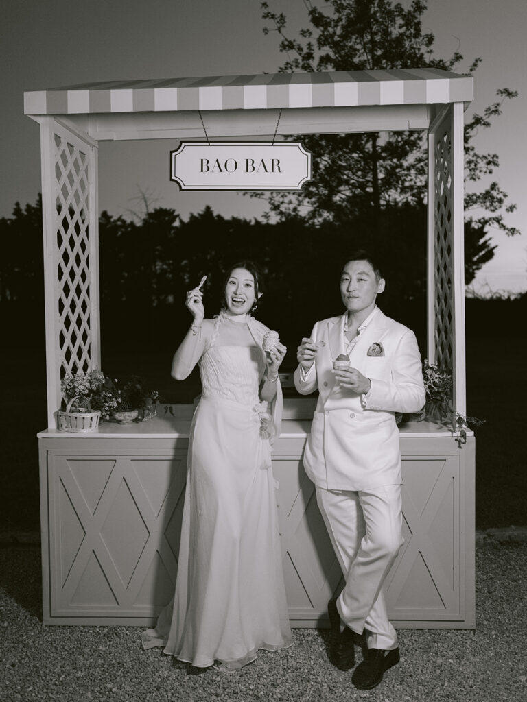 Black-and-white portrait of Casey and James enjoying bao together at the garden welcome party’s Bao Bar.
