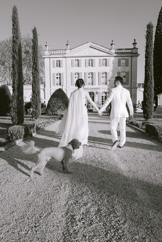 Casey and James walking hand in hand with their dog through the gardens towards Château de Tourreau.