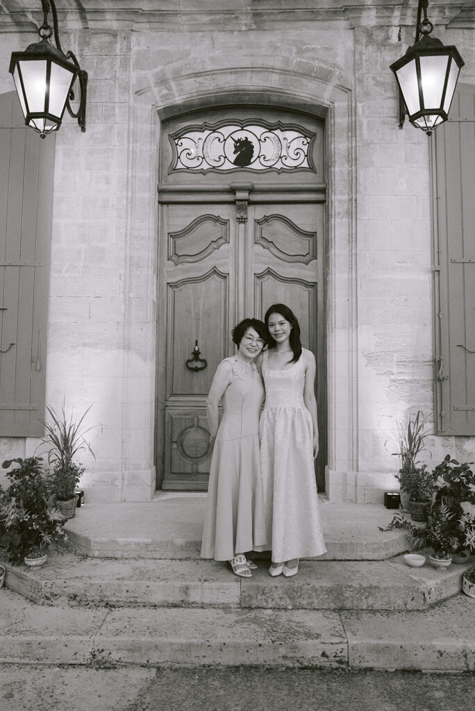 Black-and-white portrait of two guests at the illuminated entrance of Château de Tourreau, framed by botanical décor.