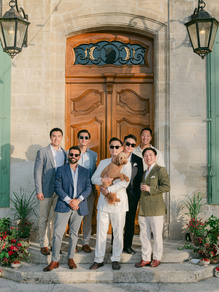 James posing with friends and the couple’s dog between red floral installations at the entrance of Château de Tourreau.