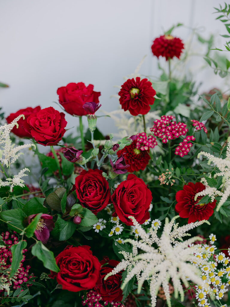 Garden-style arrangement of red roses, dahlias, burgundy flowers, astilbe and small white daisies.