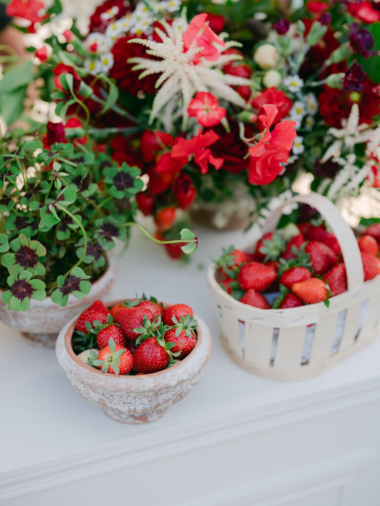 Bowls and baskets of fresh strawberries styled with oxalis and red garden flowers for the Château de Tourreau welcome event.