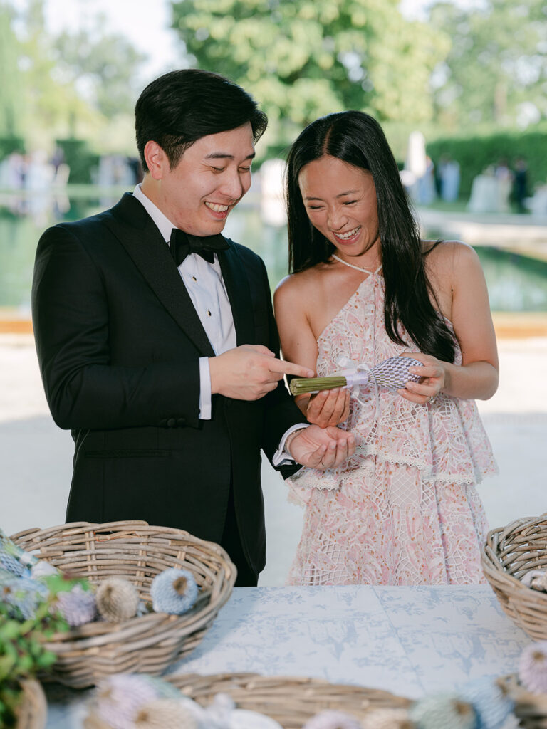 A smiling couple chooses handwoven guest fans during the garden cocktail hour at Château de Tourreau.