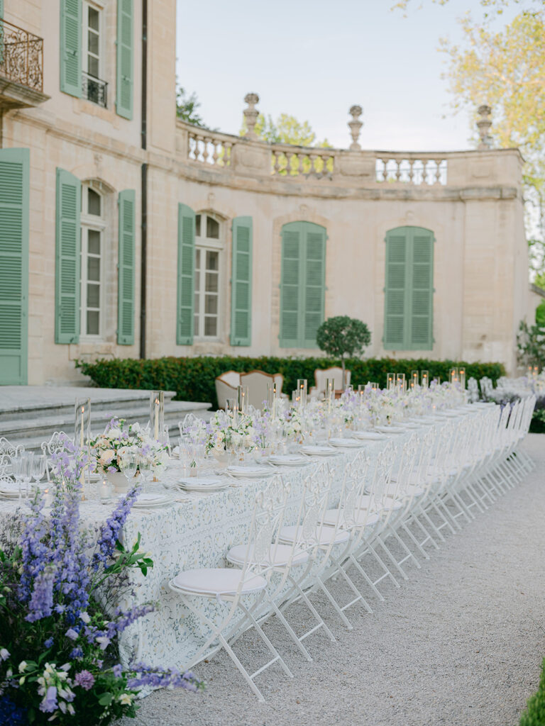 Purple garden flowers frame the corner of the long outdoor wedding tables beneath the château windows.