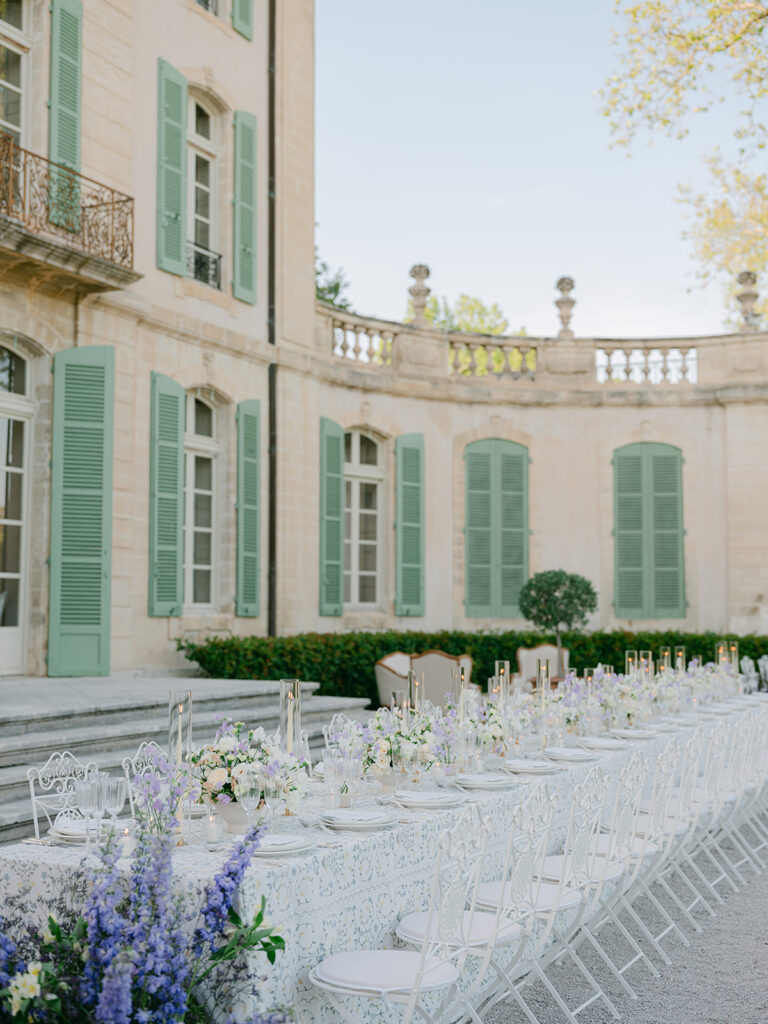 Elegant white dinner tables set beneath the pale green shutters and stone balconies of the Provence château.