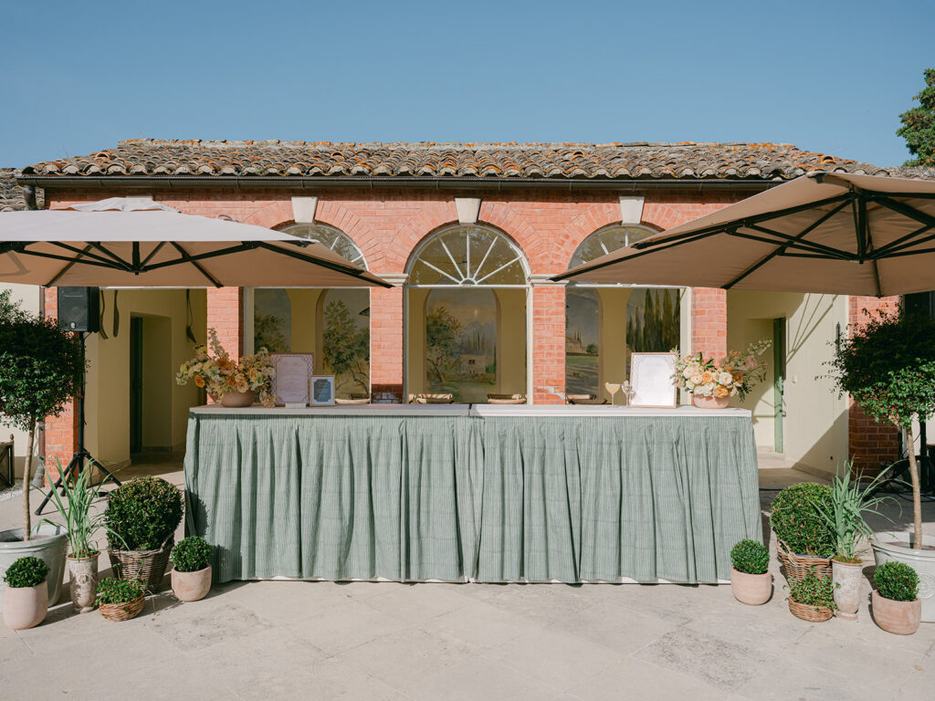 Wide view of the sage-green cocktail bar framed by potted plants and floral arrangements designed by Capucine Atelier Floral.