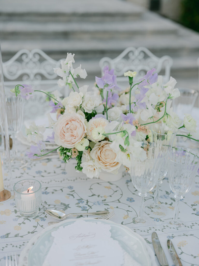 Pastel garden flowers, crystal glassware and a botanical tablecloth create a refined dinner tablescape by Capucine Atelier Floral.