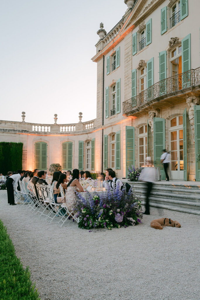 Purple and lavender flowers frame the château steps beside the outdoor dinner tables in a design by Capucine Atelier Floral.