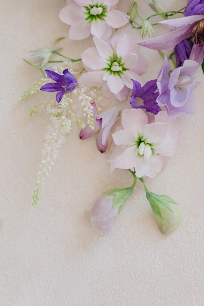 Purple sweet peas, pale hydrangea petals and delicate white blooms arranged as a romantic wedding flower detail.