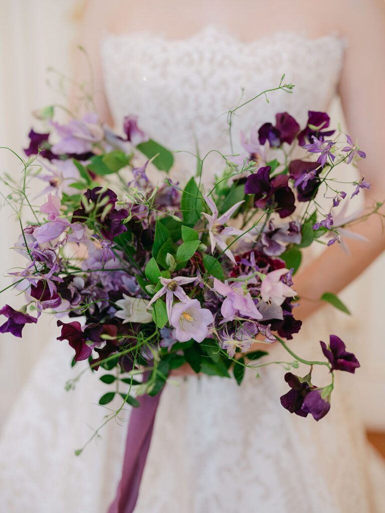 Romantic purple bridal bouquet with sweet peas, clematis and trailing greenery by Capucine Atelier Floral.