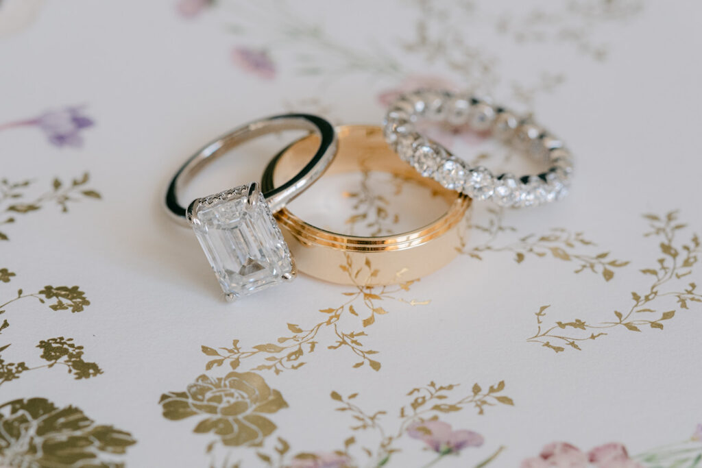 The bride and groom’s wedding rings arranged together on gold and pastel floral stationery.