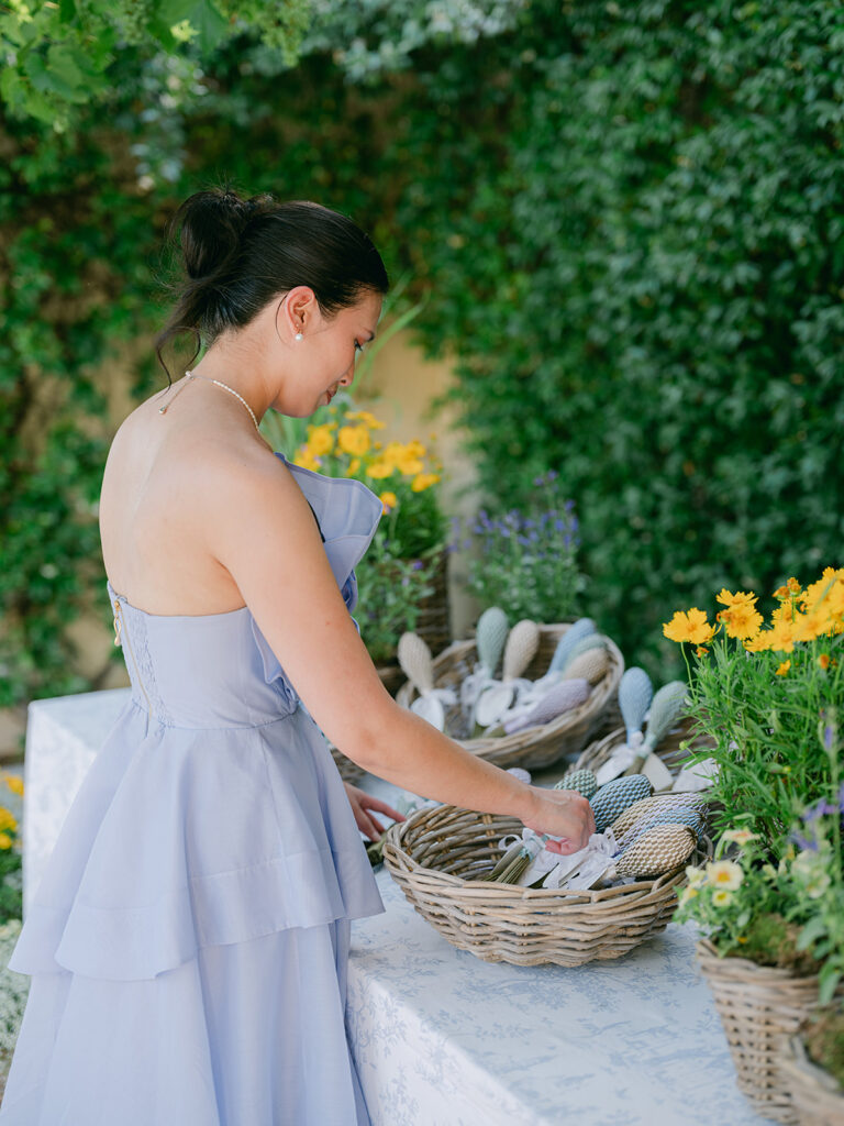 A wedding guest in a lavender dress selects a handwoven fan from a basket during the Provence cocktail hour.