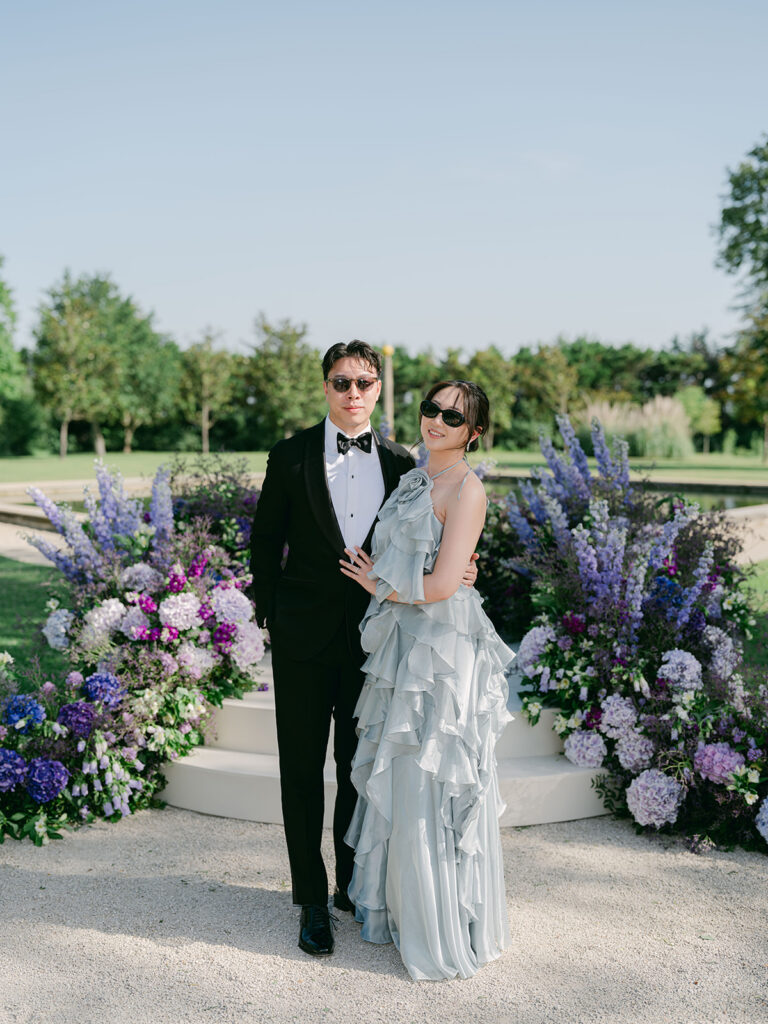 Elegant guests pose before the purple floral ceremony installation in Provence.