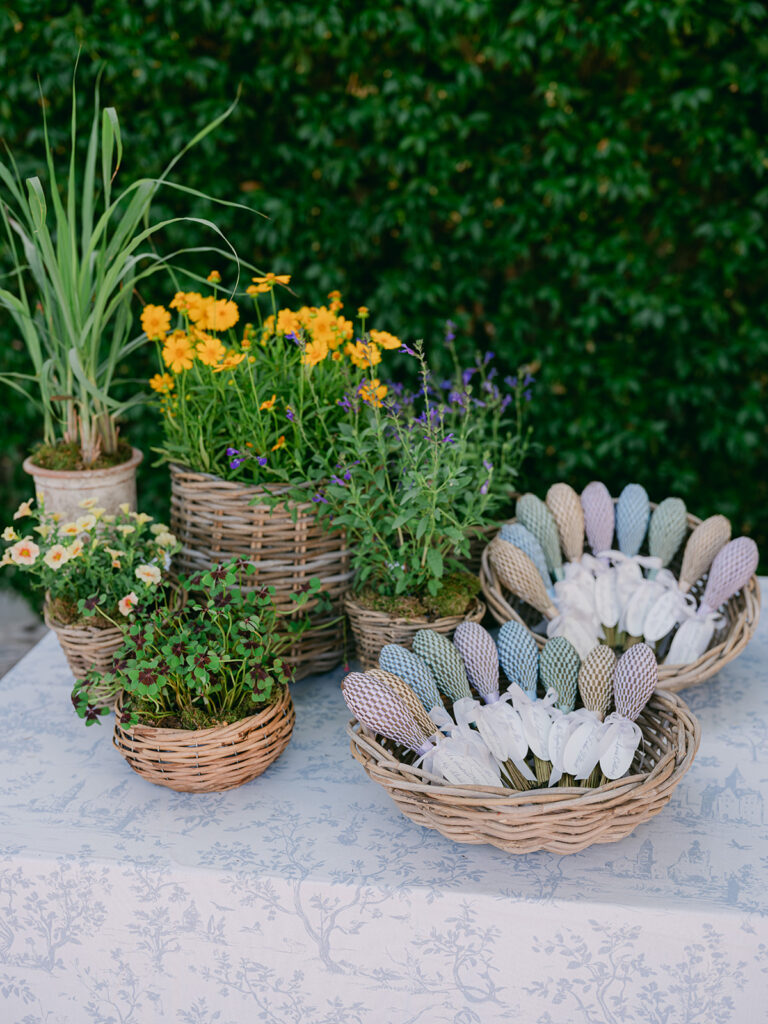 Woven baskets of patterned wedding fans displayed beside yellow flowers, lavender and potted greenery in Provence.