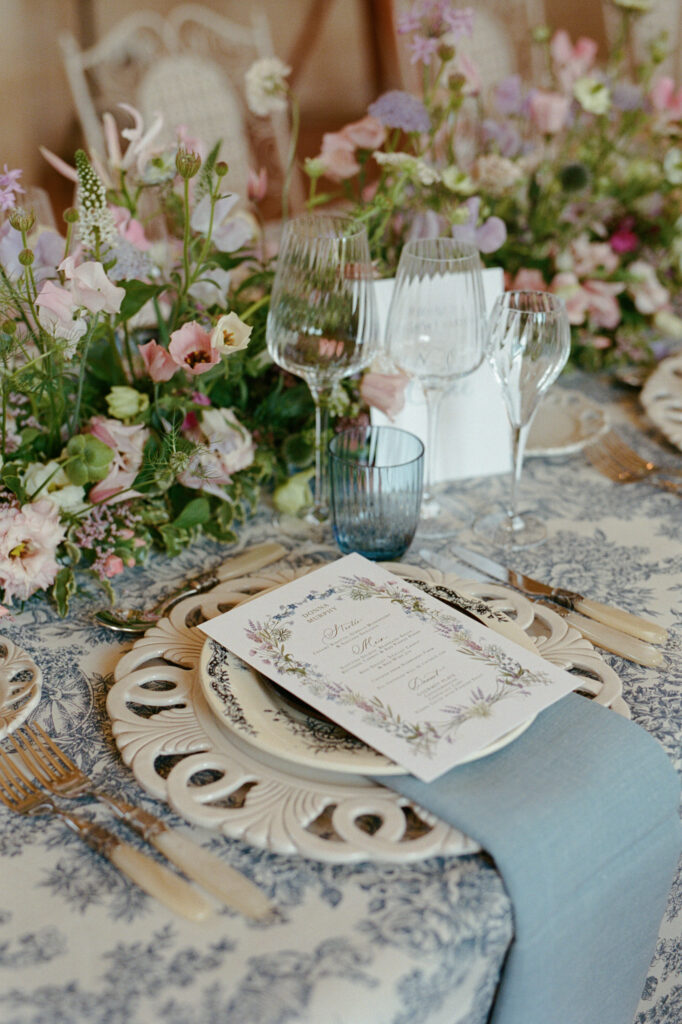 Elegant wedding place setting with blue ribbon, illustrated menu and pastel flowers at Château de Vallery.