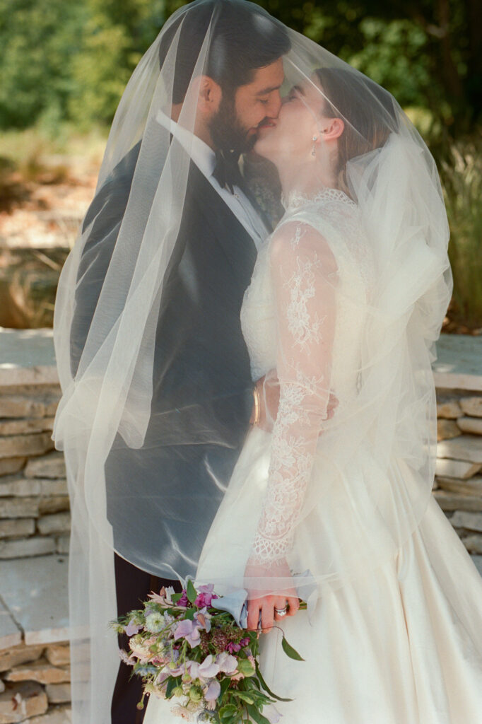 Kaylin and Paul share a kiss beneath her veil after their garden wedding ceremony at Château de Vallery.