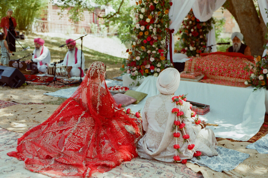 Rear view of Kaylin and Paul seated beneath the richly flowered canopy during their Sikh wedding ceremony.