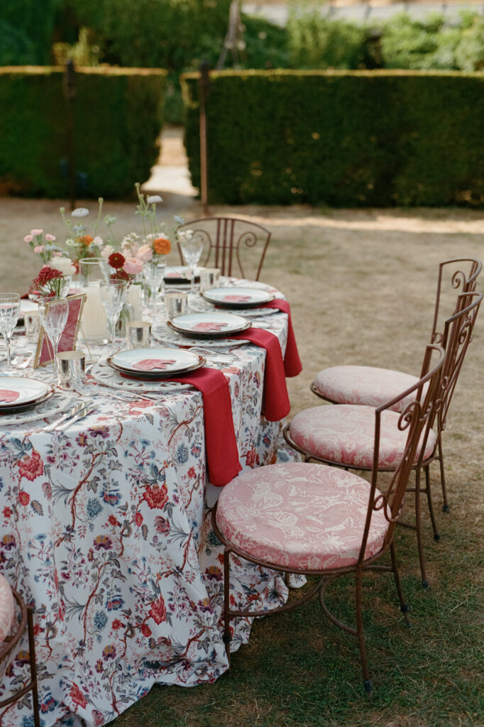 Colorful Indian wedding reception table with floral-print linen, red napkins and pink upholstered chairs.
