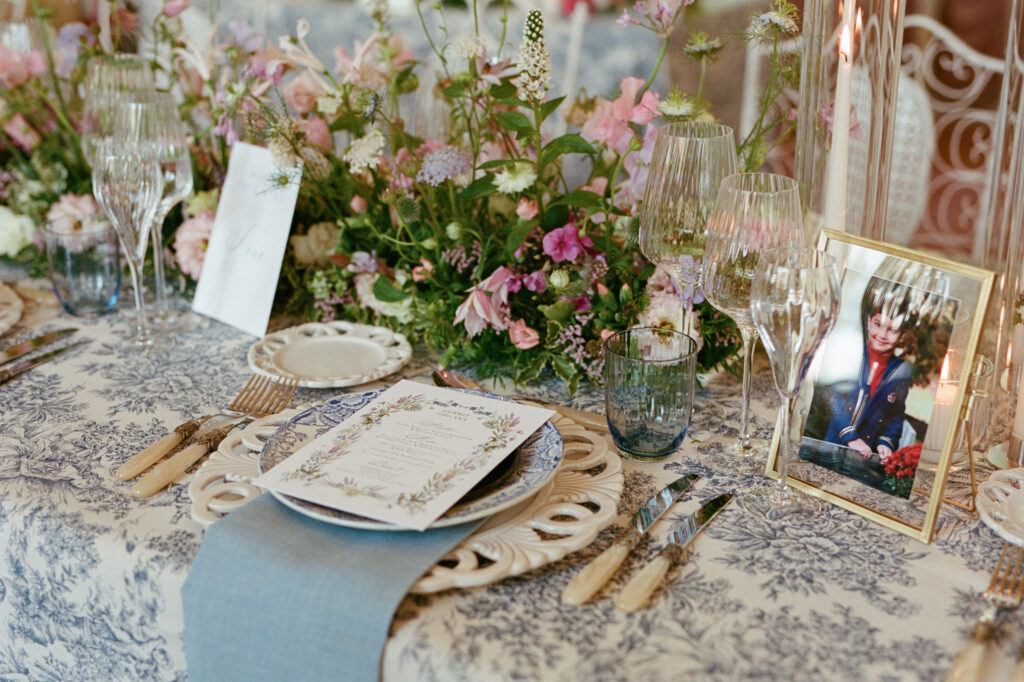 Fine-art reception table with blue toile linen, pastel floral centerpieces and layered place settings.