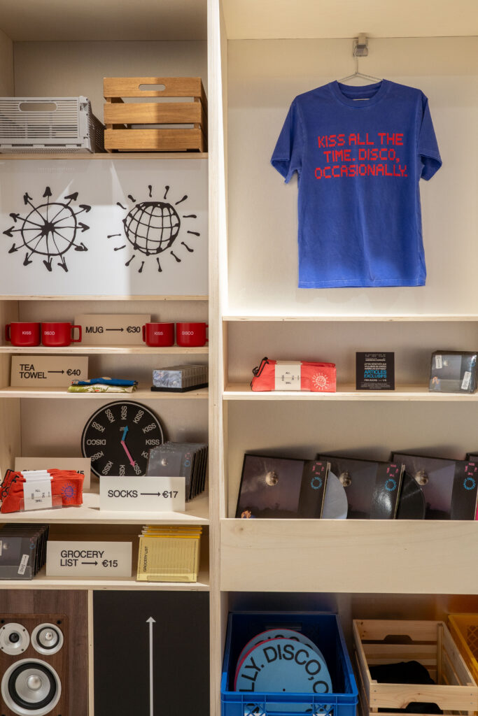 Blue album T-shirt, red mugs, socks and vinyl arranged on the merchandise wall at the Paris pop-up.