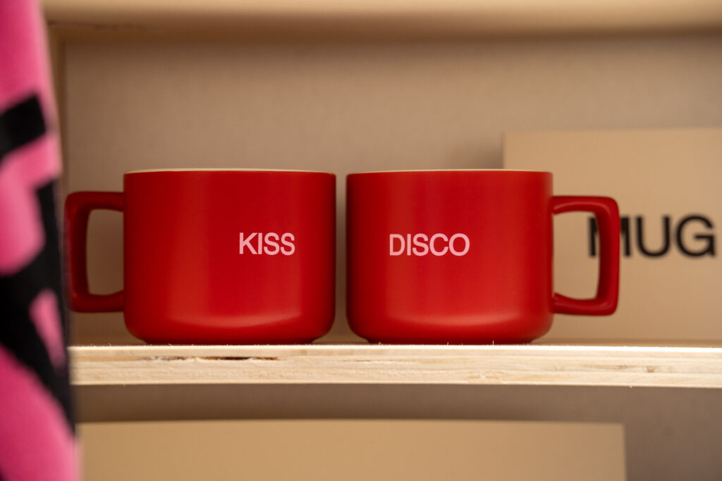 Pair of red mugs marked Kiss and Disco on a merchandise shelf at the Harry Styles Paris pop-up.