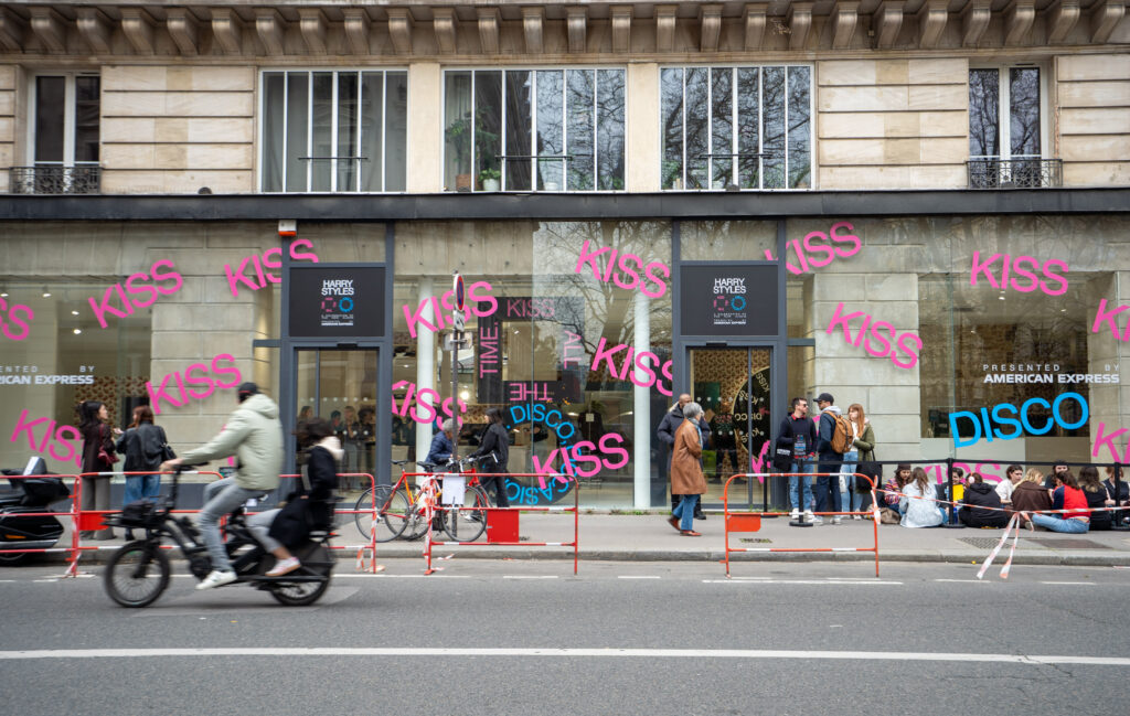 Exterior of the Harry Styles Paris pop-up with Kiss and Disco window graphics and visitors waiting outside.