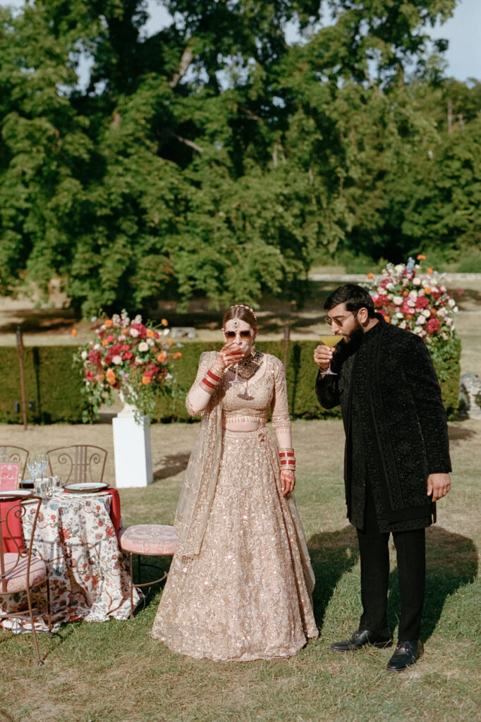 Kaylin and Paul in Indian reception attire beside colorful floral tables in the gardens of Château de Vallery.