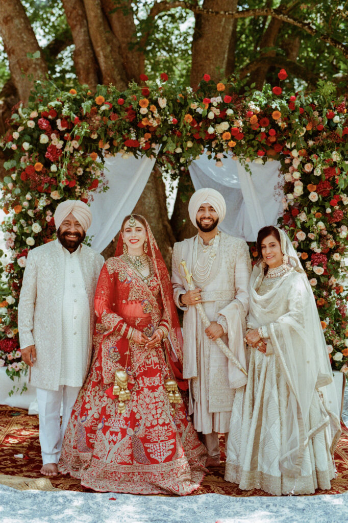 Kaylin and Paul pose with family beneath the colorful floral ceremony arch at Château de Vallery.