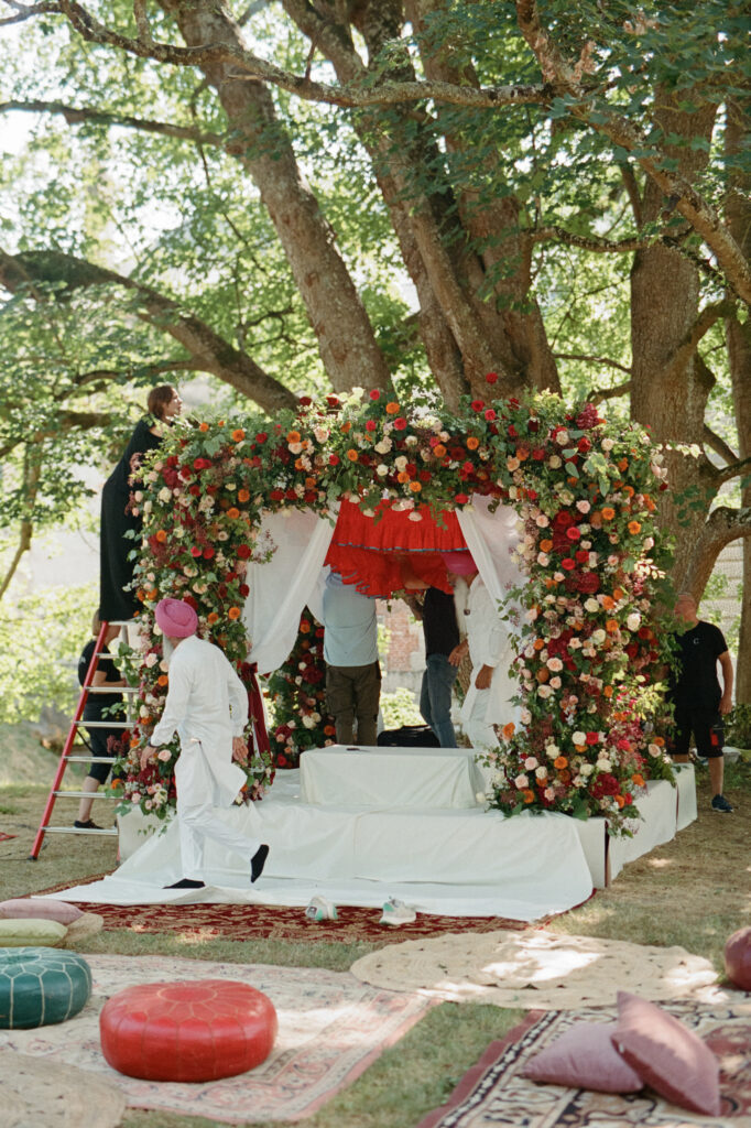 Lush red, orange, blush and cream ceremony arch by Capucine Atelier Floral beneath an old tree at Château de Vallery.