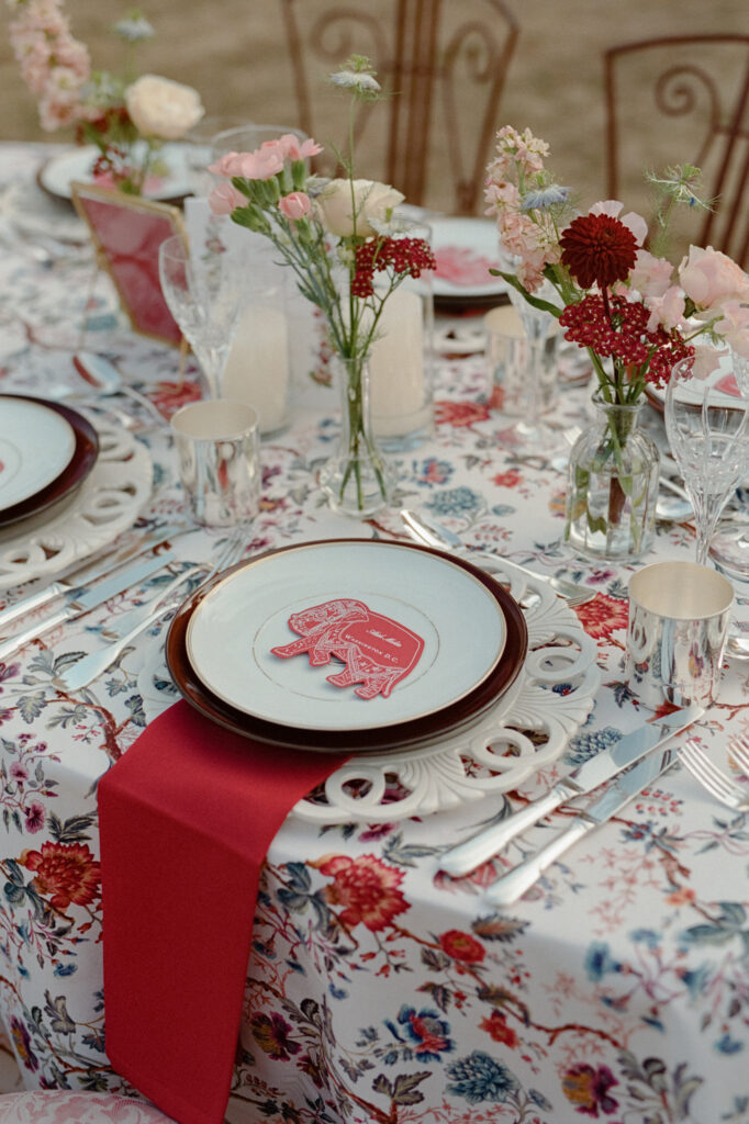Indian wedding tablescape with floral-print linen, red napkin, elephant place card and delicate bud vases.