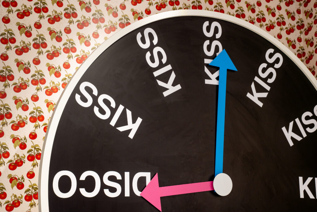 Black Kiss and Disco clock installation against tomato-patterned walls at the Harry Styles Paris pop-up.
