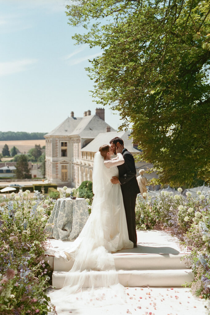 Kaylin and Paul kiss on the ceremony steps surrounded by pastel flowers overlooking Château de Vallery.