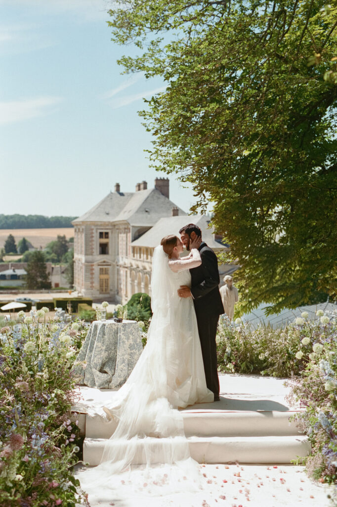 Kaylin and Paul kiss on the steps of their pastel flower-filled garden ceremony at Château de Vallery.